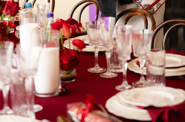 Red roses, glassware, white candles and place settings on a red tablecloth