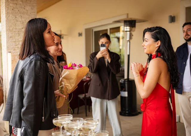 Guests greeting a woman in a red dress with a bouquet of flowers