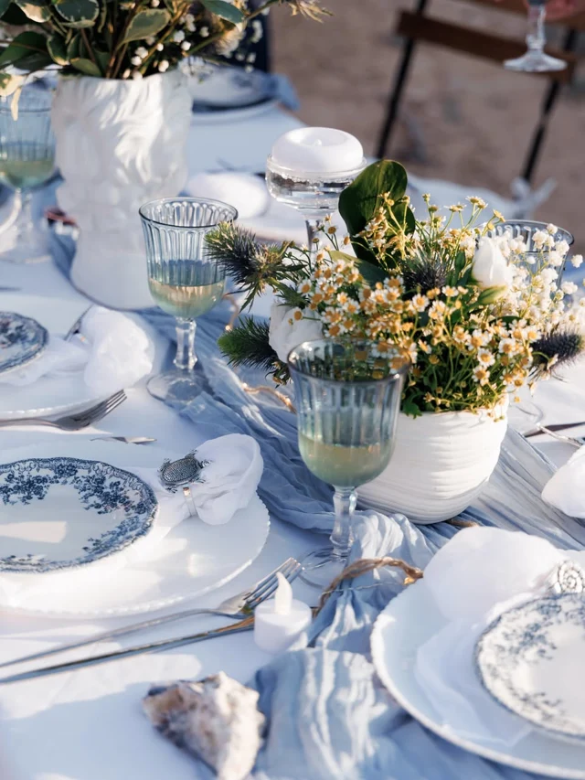 Blue glassware, white flowers and patterned plates on a seaside table