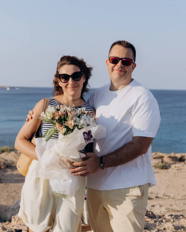 Serhiy and Anna on the coast, holding a bouquet of pale flowers
