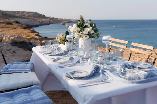 A white picnic table with blue glassware overlooking the Cyprus coastline