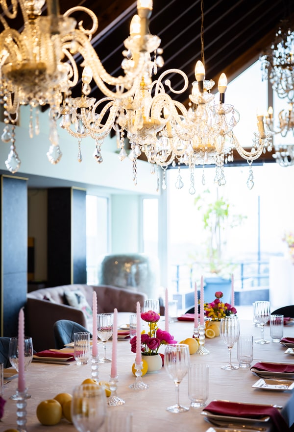 A long table with flowers, pink candles and lemons beneath chandeliers