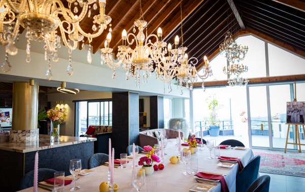 A long table with flowers, pink candles and lemons beneath chandeliers