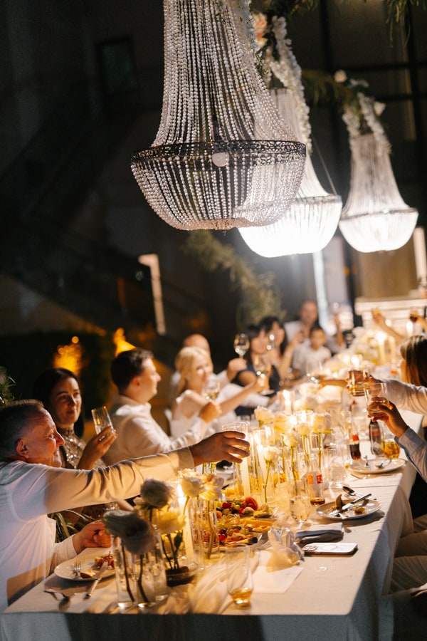 Guests dining beneath illuminated chandeliers after dark