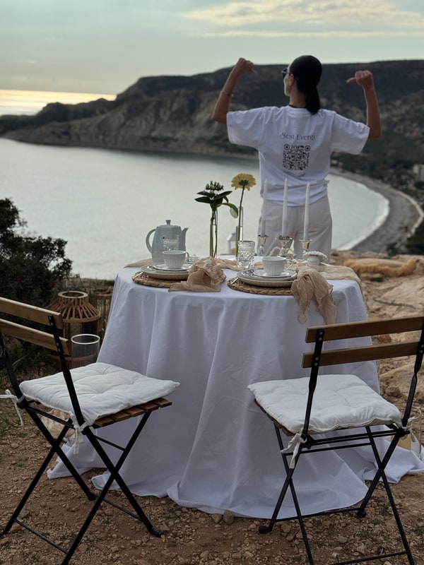 A woman standing beside the picnic table with the coast behind her