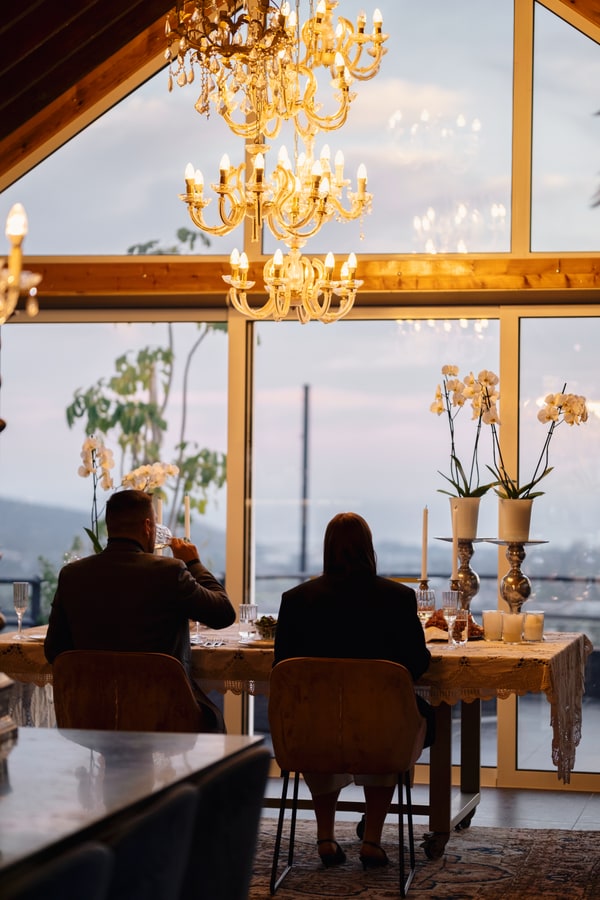 A couple at a candlelit table beside large windows