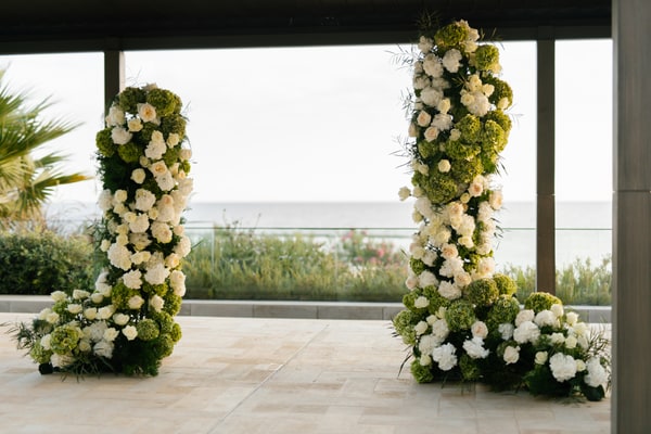 Two tall floral arrangements framing a sea view at the ceremony pavilion