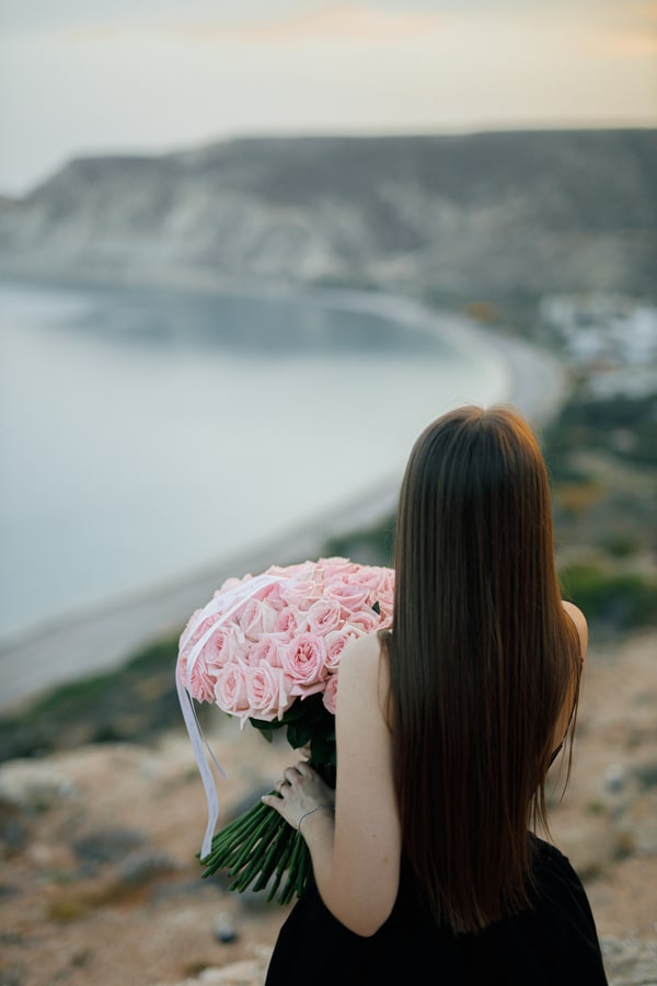 A woman holding pink roses with the bay behind her