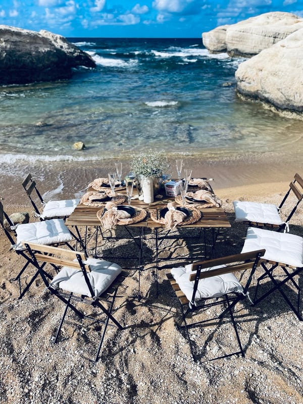 A picnic table with woven placemats and glassware beside the sea