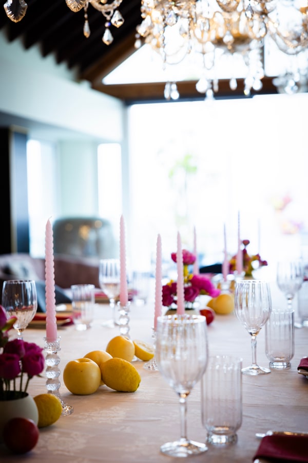 A long table with flowers, pink candles and lemons beneath chandeliers