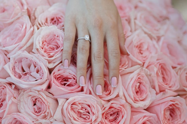 An engagement ring on a hand resting on pink roses