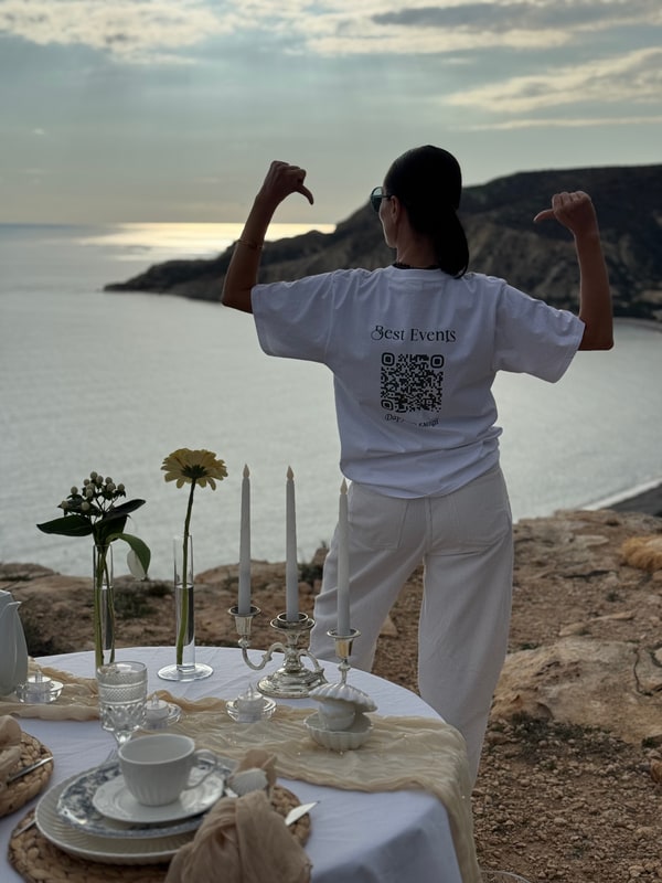 A woman standing beside the picnic table with the coast behind her