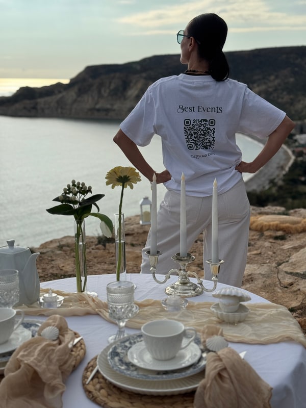 A woman standing beside the picnic table with the coast behind her