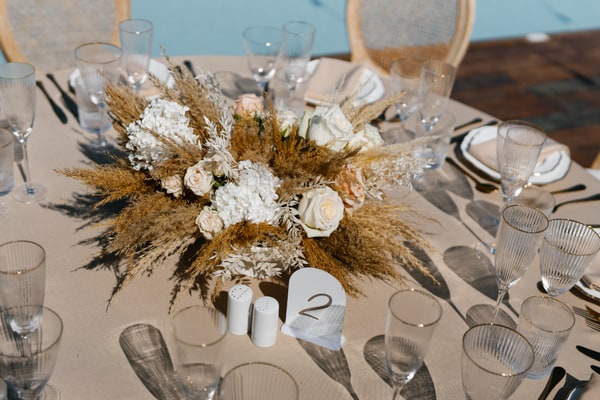 White flowers, dried grasses and ribbed glasses on a wedding table