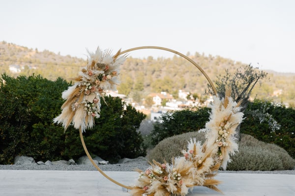 A circular ceremony arch with pale flowers and dried grasses overlooking the hills