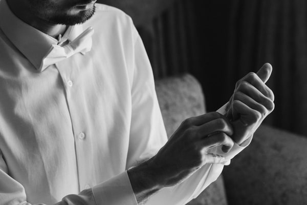A groom fastening the cuff of his white shirt