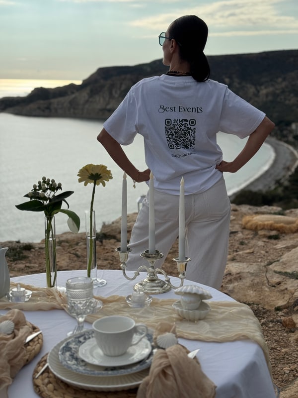 A woman standing beside the picnic table with the coast behind her