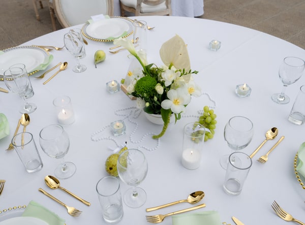 White plates, gold-coloured cutlery and green floral details on a reception table