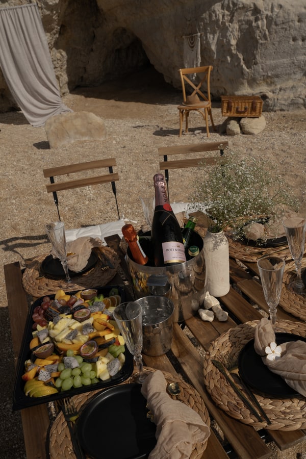 A picnic table with woven placemats and glassware beside the sea