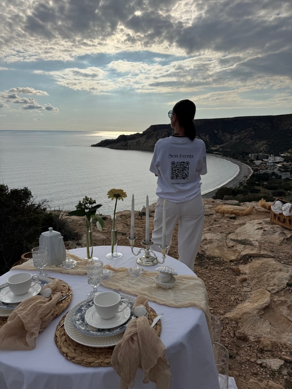 A woman standing beside the picnic table with the coast behind her