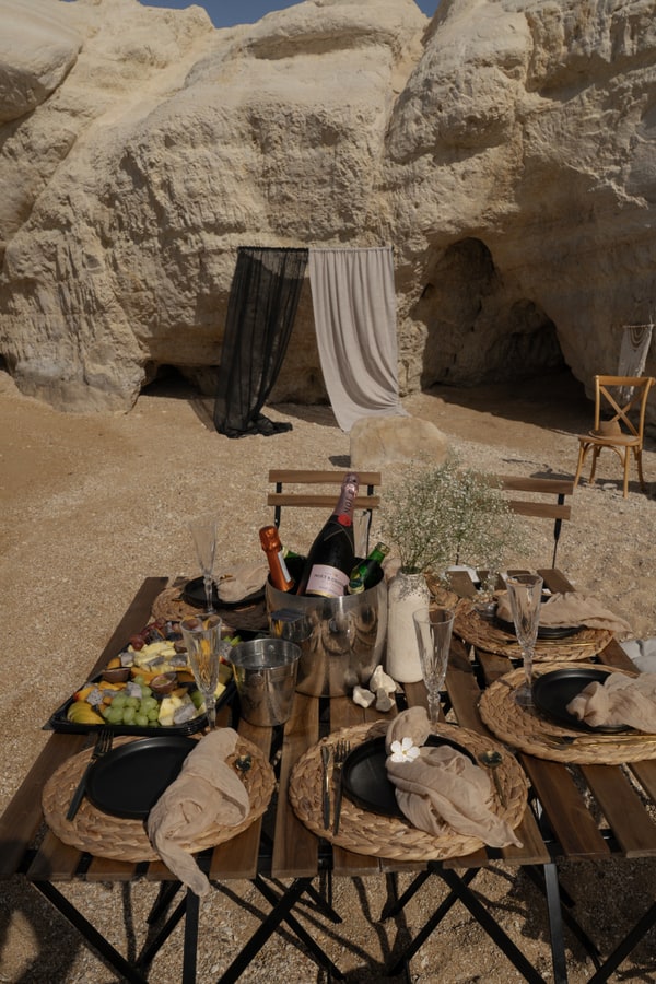 A picnic table with woven placemats and glassware beside the sea