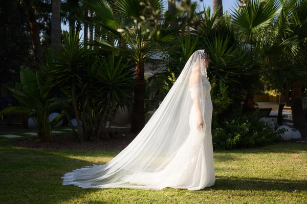 A bride in a flowing veil beside the garden and pool