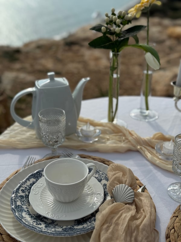 A seaside picnic table with teacups, pale fabric and candles