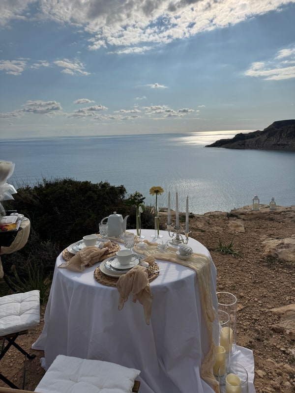 A seaside picnic table with teacups, pale fabric and candles