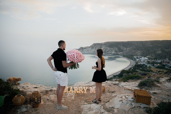 A man holding pink roses beside his partner and Marry Me letters