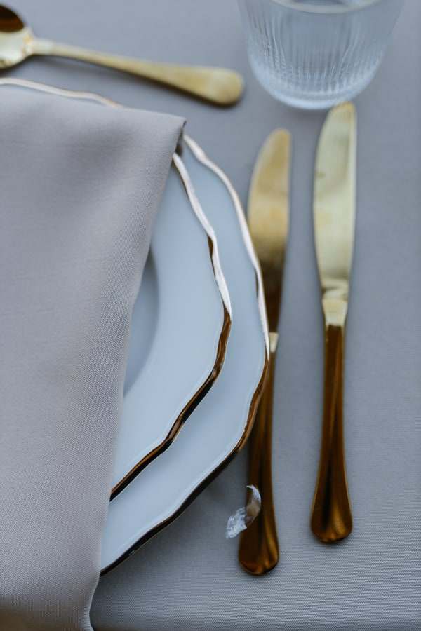 A softly folded napkin and gold-coloured cutlery on a white place setting