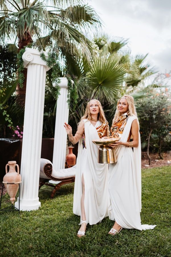 Two performers in white costumes standing beside columns