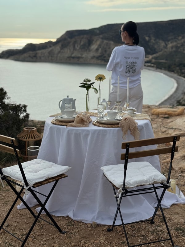 A woman standing beside the picnic table with the coast behind her