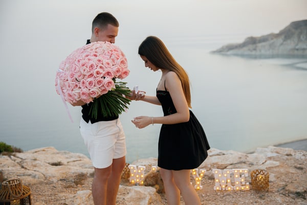 The couple looking at the engagement ring beside the roses