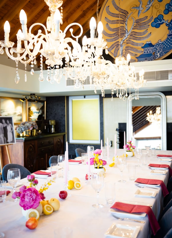 A long table with flowers, pink candles and lemons beneath chandeliers