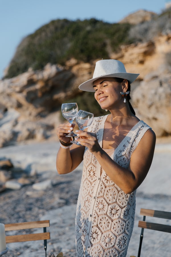 A woman in a white hat holding a glass beside the sea
