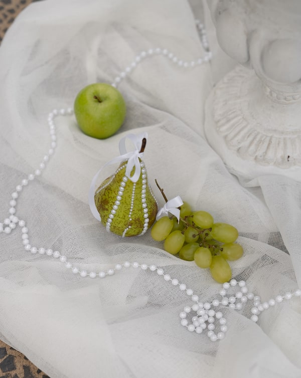 Pearls, a green pear and grapes arranged on soft white fabric