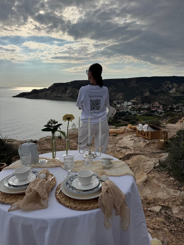 A woman standing beside the picnic table with the coast behind her