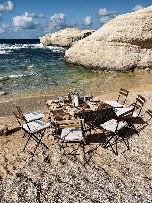 A picnic table with woven placemats and glassware beside the sea