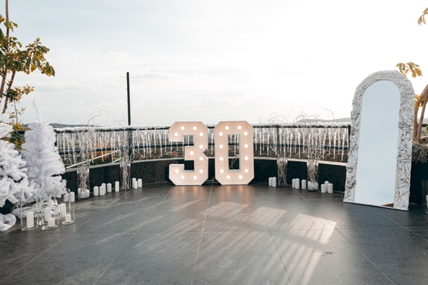 Illuminated number 30 beside white winter decorations on a terrace