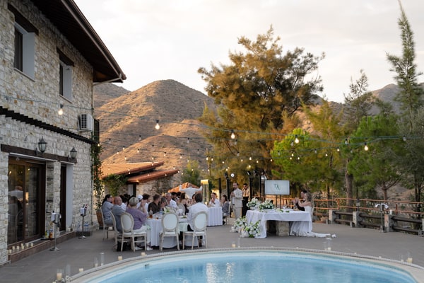 Poolside reception tables beside a stone building in the evening light