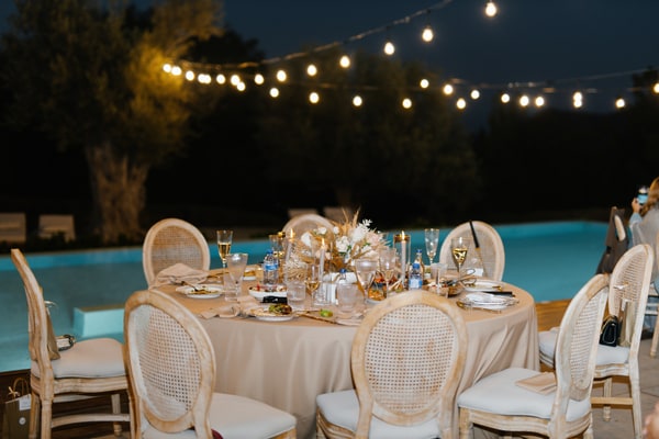 A candlelit reception table beneath glowing festoon lights at dusk