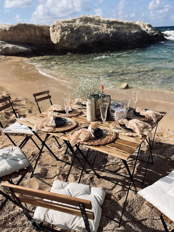 A picnic table with woven placemats and glassware beside the sea