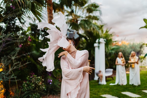 A performer with a large floral headpiece beside the pool