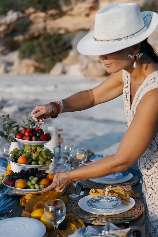 A woman in a white hat arranging fruit on the seaside table
