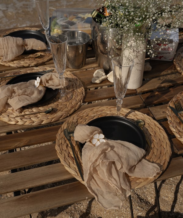 A picnic table with woven placemats and glassware beside the sea