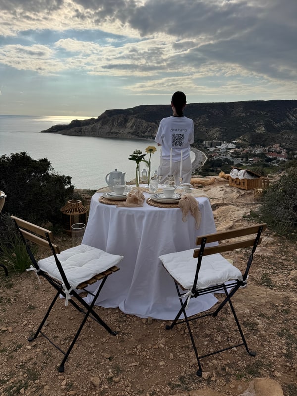 A woman standing beside the picnic table with the coast behind her