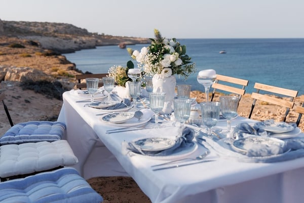 A white picnic table with blue glassware overlooking the Cyprus coastline