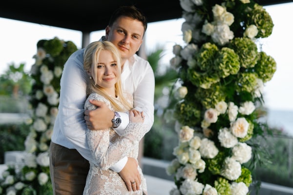 Valeria and Anatoly embracing beside white and green ceremony flowers