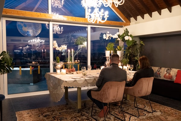 A couple at a candlelit table beside large windows