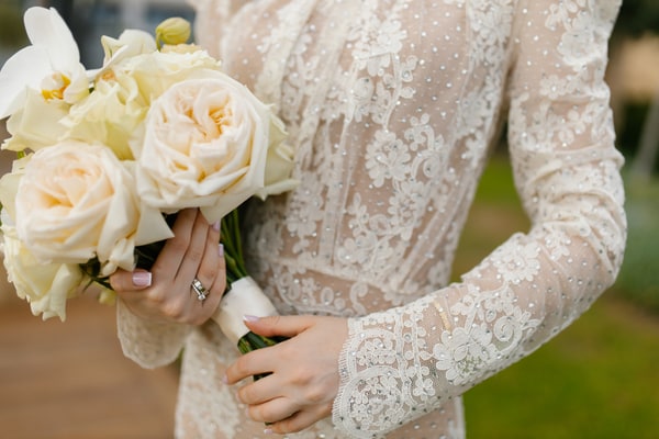 Valeria holding a white rose bouquet against her lace wedding dress